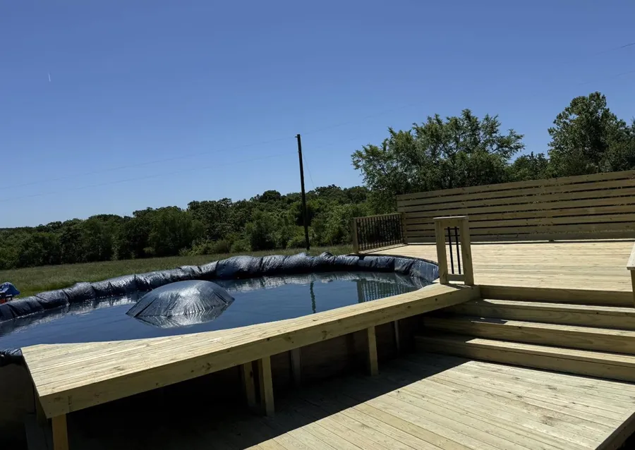 Raised wood pool deck with wraparound steps and horizontal-slat privacy wall around an above-ground pool in NWA — JHG Contracting LLC